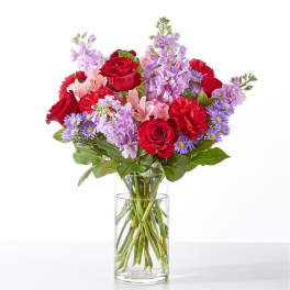Bouquet of red roses, purple flowers, and pink blooms in a clear glass vase
