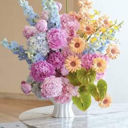 Colorful bouquet of pink, blue, and peach flowers in a white vase