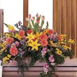 Large mixed floral arrangement with yellow lilies and pink blooms on a casket