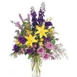 Mixed bouquet with yellow lilies, purple flowers, and pink roses in a clear vase
