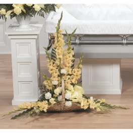 Yellow floral funeral spray on a wicker base beside a casket