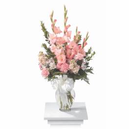 Pink gladiolus and carnations in a clear glass vase with a white ribbon