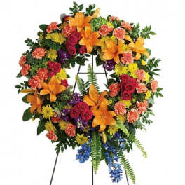 Bright multicolor standing wreath with lilies, roses, carnations, and mums on a metal easel.