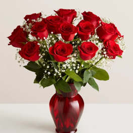 Red roses arranged in a red glass vase with baby's breath