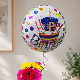 Birthday balloon above a small bouquet of colorful gerbera daisies in a glass vase