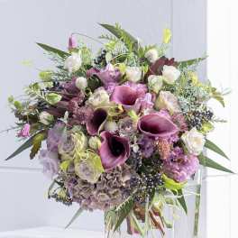 Bouquet of purple calla lilies, roses, and hydrangeas in a clear glass vase