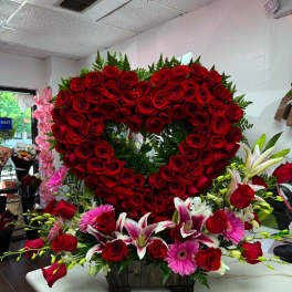 Heart-shaped red rose arrangement with pink lilies and gerbera daisies in a wooden container