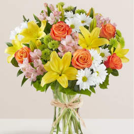 Bouquet of yellow lilies, orange roses, and white daisies in a glass vase