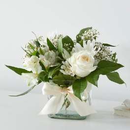 White roses and lilies arranged in a glass vase with a ribbon
