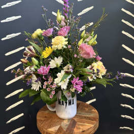 Mixed pastel bouquet in a white mug vase on a wooden stool
