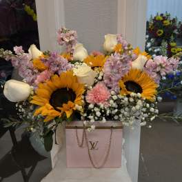Bouquet of sunflowers, white roses, and pink flowers in a pink gift bag