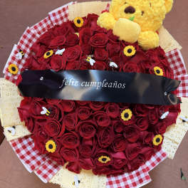 Heart-shaped red rose bouquet with a yellow teddy bear and birthday ribbon