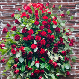 Large bouquet of red roses and carnations with greenery against a brick wall