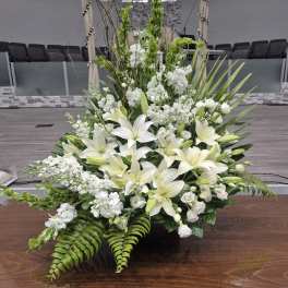 Large white floral arrangement with lilies and greenery in a church setting