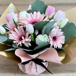 Bouquet of pink gerbera daisies and white tulips wrapped in gold and pink paper