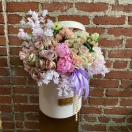 Pastel roses and pink peonies in a round cream hatbox with purple ribbon and pearls