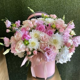 Pink and white flower arrangement with roses in a pink hatbox with ribbon bow
