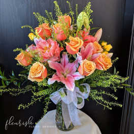Pink lilies and peach roses in a glass vase with a white ribbon