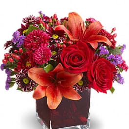 Red and orange mixed flower arrangement in a square glass vase