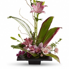 Pink lilies and orchids arranged in a black vase with tropical leaves