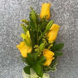 Yellow roses and lilies in a clear glass vase with a ribbon