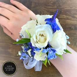 White rose and blue flower wrist corsage with ribbon on a person’s wrist