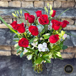 Tall arrangement of red roses with white accent flowers in a clear glass vase