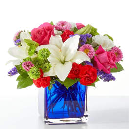 Bouquet of pink roses, white lilies, and mixed flowers in a blue glass vase