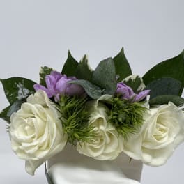 White roses with purple blooms and greenery in a white box