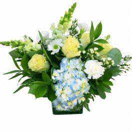 Yellow roses and blue hydrangeas in a low glass vase