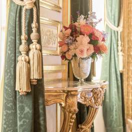 Pink and peach flower arrangement in a silver vase on an ornate table