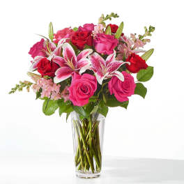 Pink and red roses with lilies in a clear glass vase