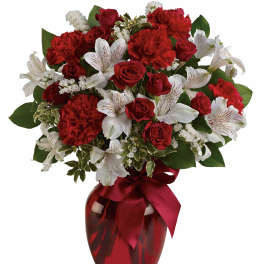 Red roses and white lilies in a red glass vase with a ribbon