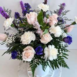 Bouquet of pale pink roses, white carnations, and purple flowers in a white vase