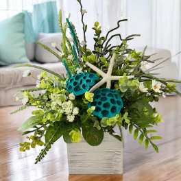 Tropical floral arrangement in a white square vase with starfish accents