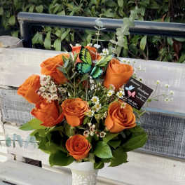 Orange roses arranged in a white vase with small white filler flowers.