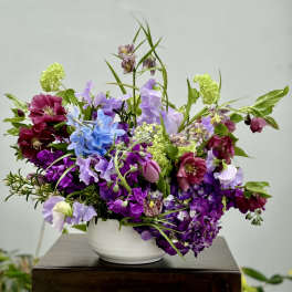Mixed purple and blue floral arrangement in a white bowl vase