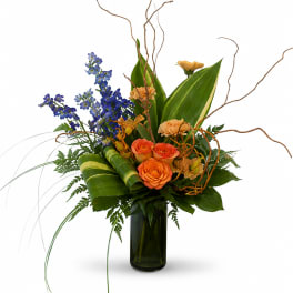 Orange roses and blue flowers in a tall glass vase with curly branches