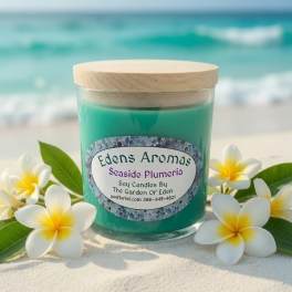 Teal candle in a glass jar with a wood lid, surrounded by white plumeria flowers
