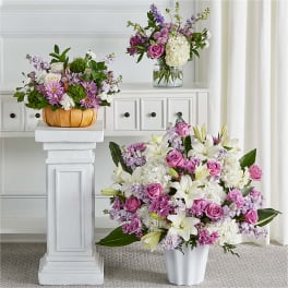 Three floral arrangements with pink, white, and purple flowers in vases and a pumpkin container.