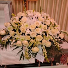 Large white and cream casket spray of roses and lilies in front of a wooden crucifix