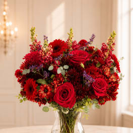 Red roses and mixed red flowers in a clear glass vase