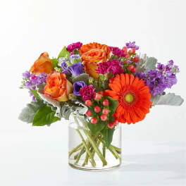 Mixed bouquet of orange, purple, and pink flowers in a clear glass vase