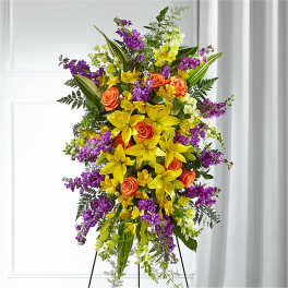 Tall standing floral spray with yellow lilies, orange roses, and purple flowers