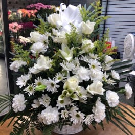 White floral arrangement in a white basket with daisies, roses, lilies, and carnations