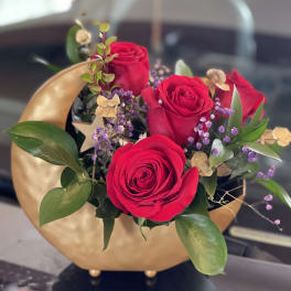 Red roses arranged in a gold vase with purple filler flowers