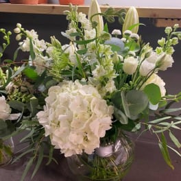 White floral arrangement in a clear glass vase with mixed greenery