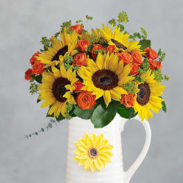 Sunflowers and orange roses arranged in a white pitcher vase