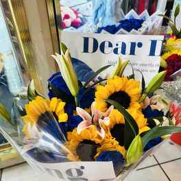 Bouquet of sunflowers, blue roses, and lilies wrapped in clear plastic