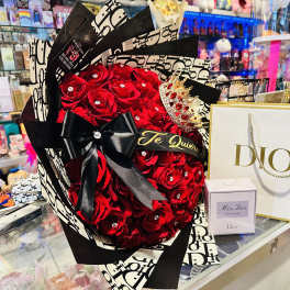 Red rose bouquet with a black ribbon beside a Dior gift bag and perfume box